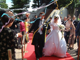 花嫁と花婿が赤いカーペットの中を進み、招待客が紙テープを投げて祝福しています。
