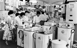 電器店で数人の男性と女性が並んだ洗濯機を見ています。