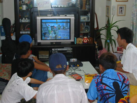 A group of boys sit facing the TV, playing computer games