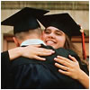 The back of a man hugging a woman, both wearing black gowns and mortar boards.