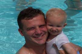 プールの中で小さな子供を抱えた父親が、ニコニコ笑っています。