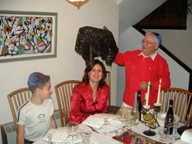 正装したユダヤ人家族が、キャンドルがともり、ワインもおかれたダイニングテーブルを囲んでいます。