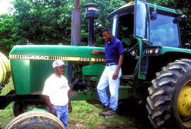 Two African American men stand by a green tractor.